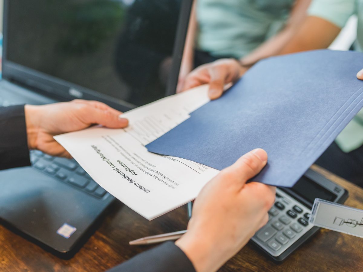 Broker handing a client a navy folder with a residential mortgage application